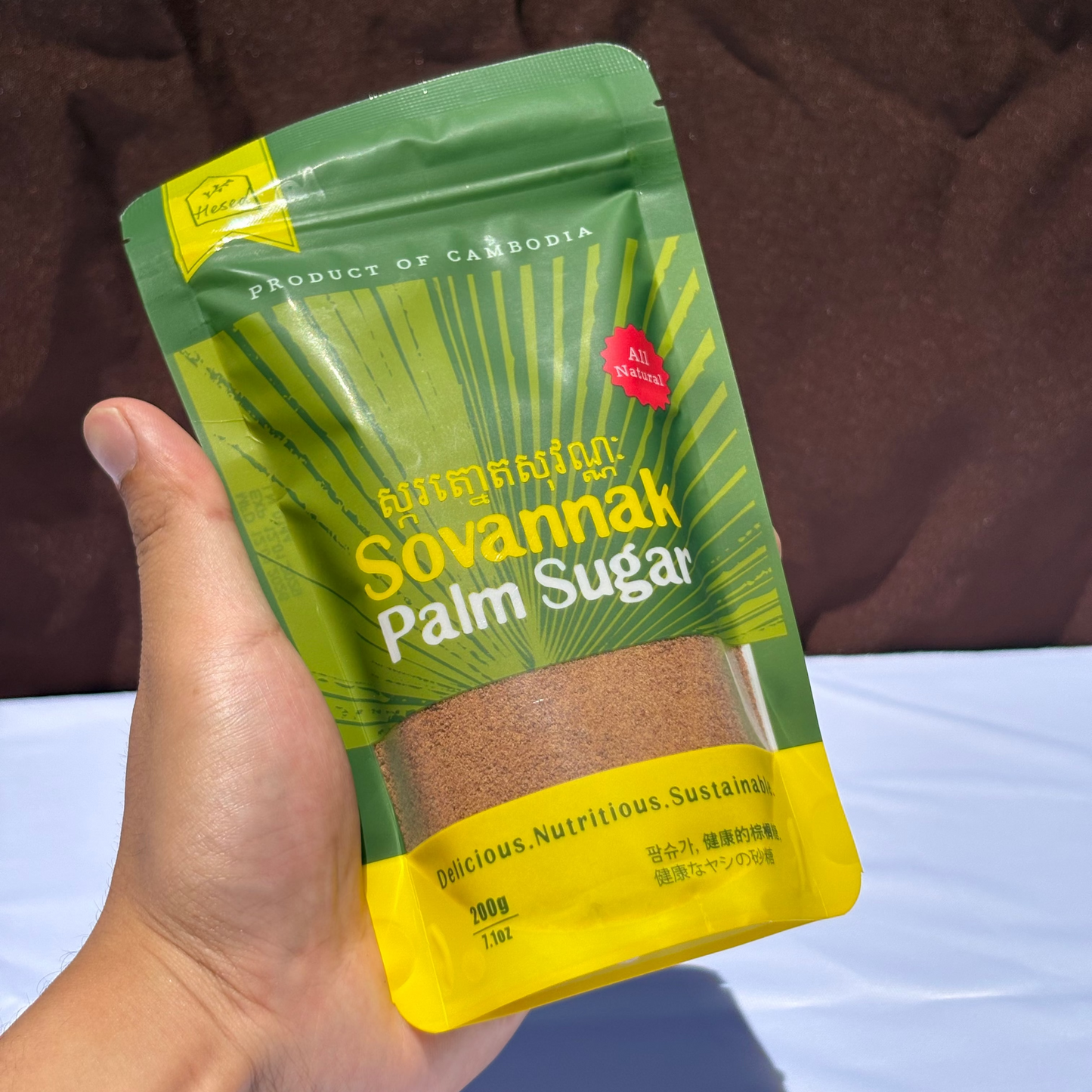 Hand holding a package of Sovannak Palm Sugar with a green and yellow design.